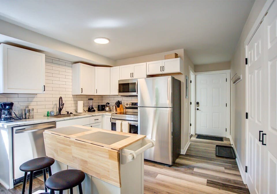 Modern kitchen with stainless steel appliances, subway tile backsplash, and a movable island with seating for two. Bright and open layout flows seamlessly to the entryway for easy access and convenience.