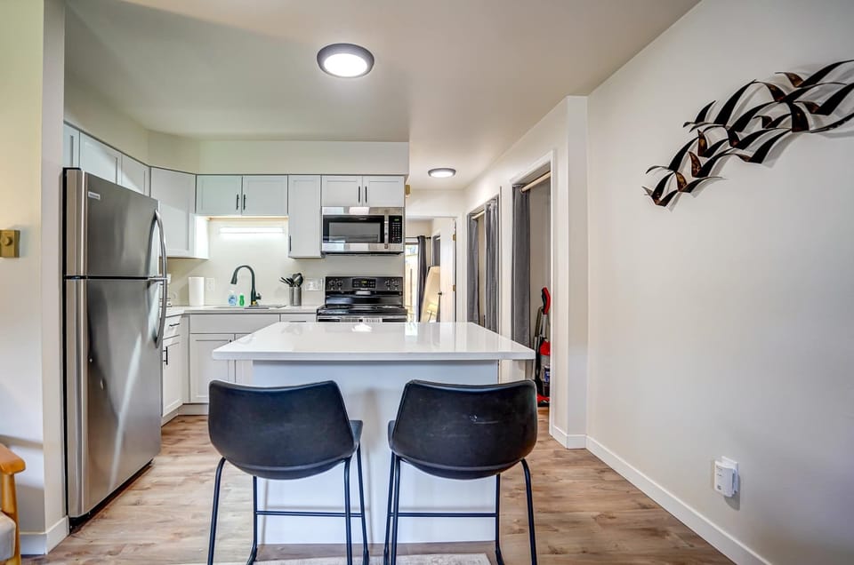 Contemporary kitchen with stainless steel appliances, sleek white cabinetry, and a spacious island with seating for two. Perfect for cooking, dining, or simply enjoying a relaxed morning coffee in a clean, modern setting.