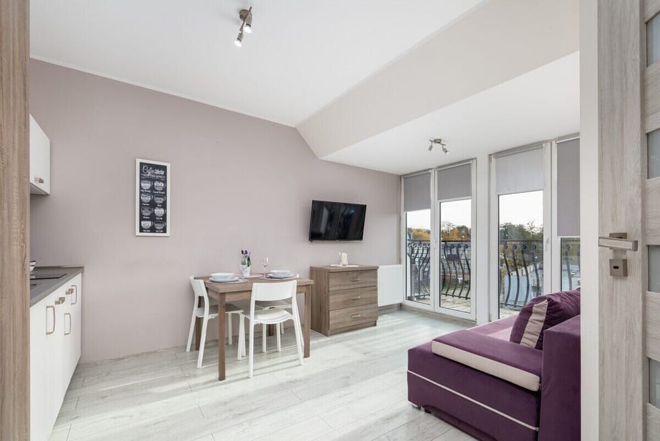 An open-plan living area with a purple sofa, dining table, and kitchen in a neutral color scheme.

