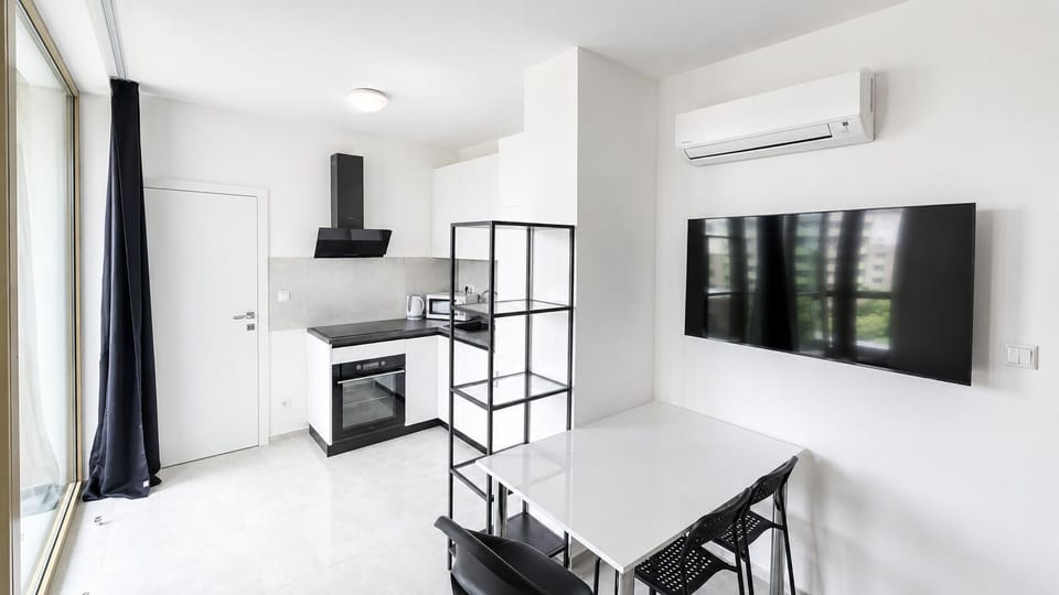 Bright modern studio with kitchenette, AC, dining area, and wall-mounted TV