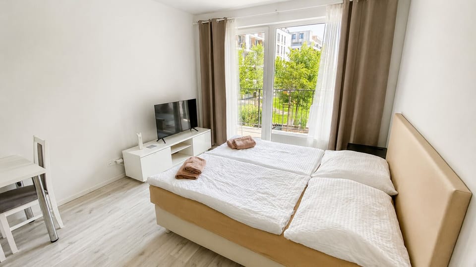 Bright bedroom with balcony views, natural light, and TV