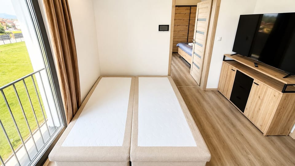 Bright twin bedroom with balcony views, natural light, and TV