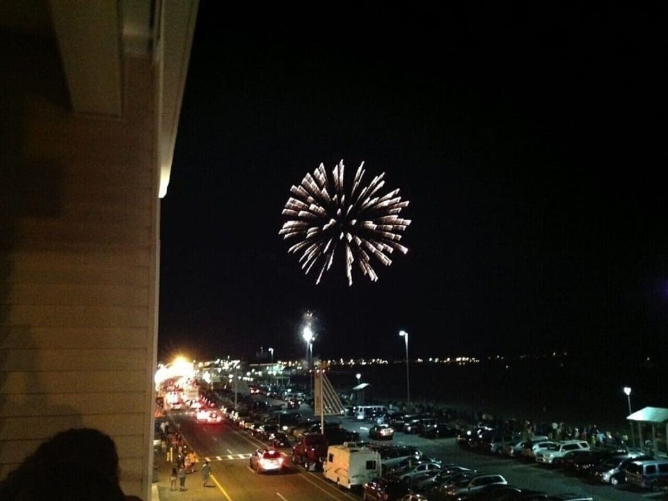 Fireworks bursting over the shoreline, watched from the deck on a summer night.