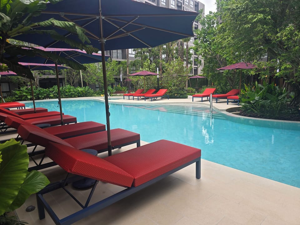 Resort-style pool with tropical gardens, loungers, and shaded seating
