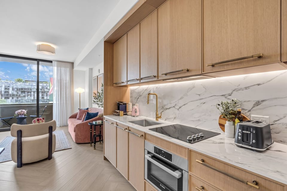 Fully equipped open kitchen with electric cooktop, built-in oven, marble backsplash and breakfast counter — everything you need for a home-cooked meal