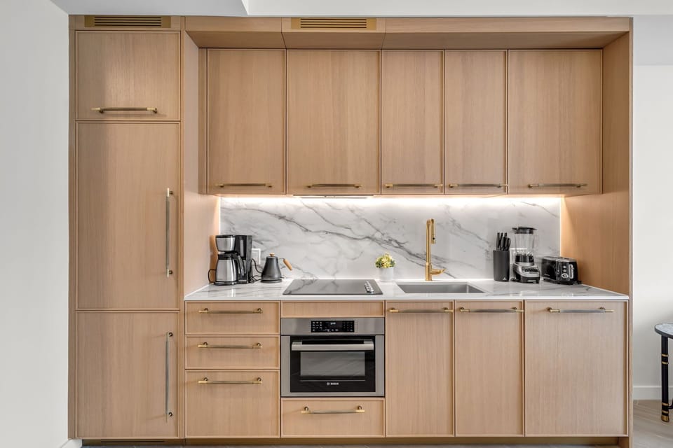 Sleek modern kitchen with warm wood cabinetry, quartz countertops, built-in appliances and gold fixtures — beautifully designed for cooking in style