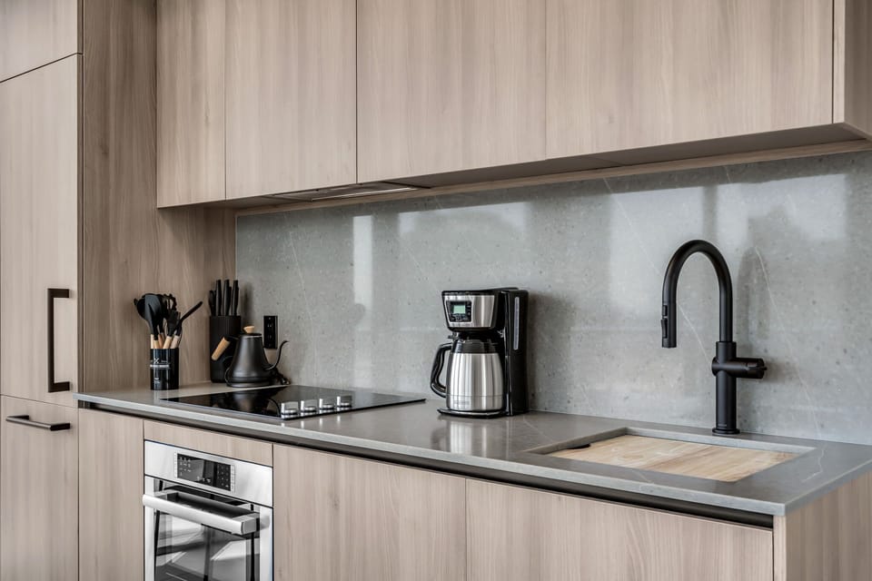 Sleek and functional! This designer kitchen features premium integrated appliances, warm wood cabinetry, and a seamless stone backsplash. Perfectly equipped with a modern induction cooktop and matte black fixtures for a high-end feel.