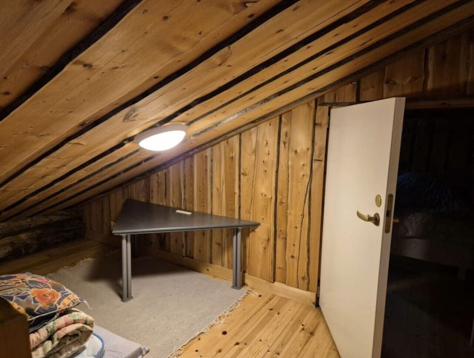 Open loft area with a low sloping ceiling, a table and a doorway to a sleeping alcove.