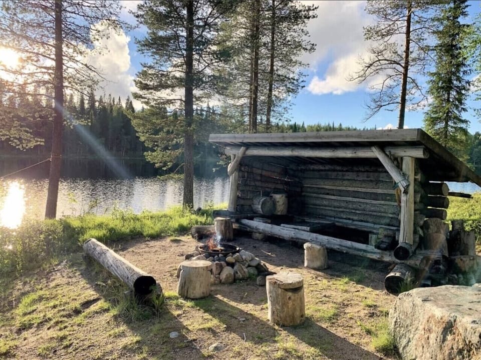 Shared log lean-to shelter with an open fire pit on the lakeshore.