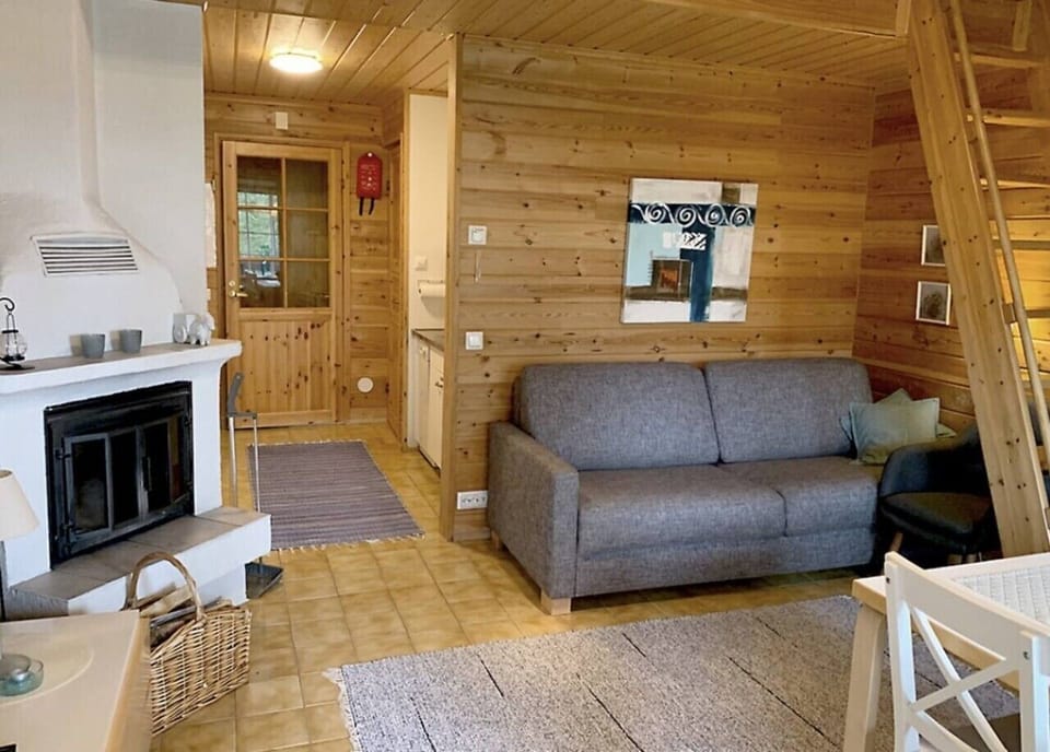 Log-walled living room with a fireplace, a sofa bed and stairs up to the loft.