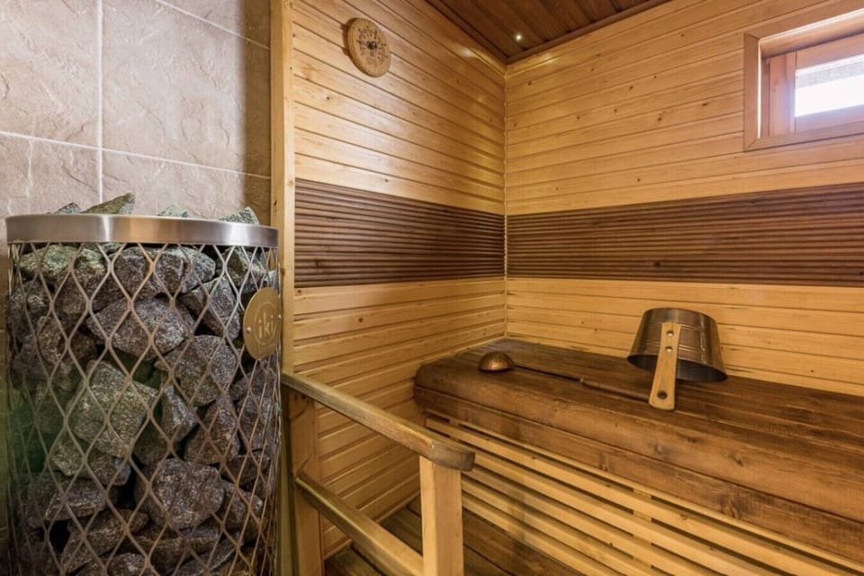 Private electric sauna with wooden benches and a traditional sauna bucket and ladle.