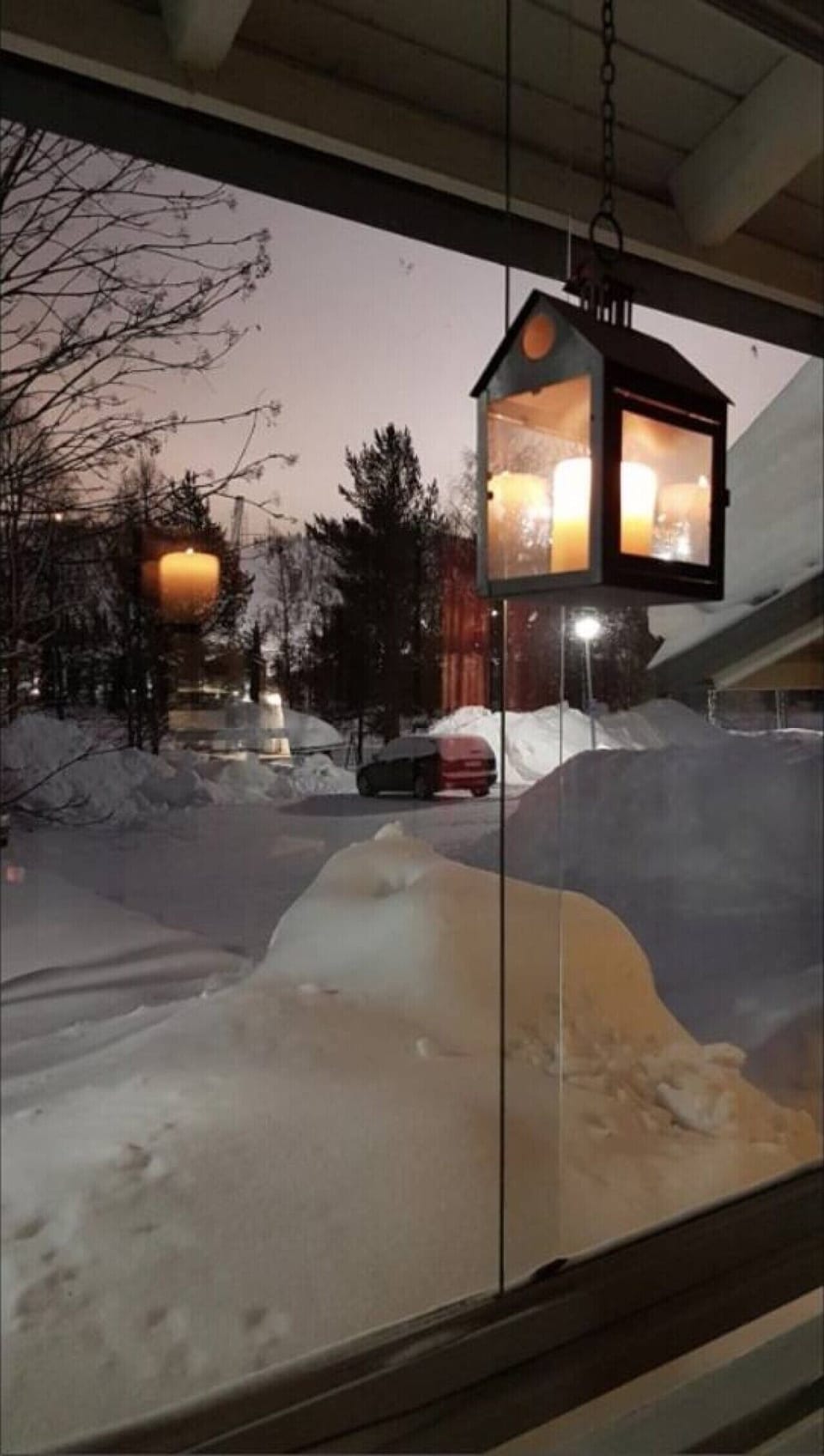 Snow-covered yard and parking area seen from the lit terrace at night.