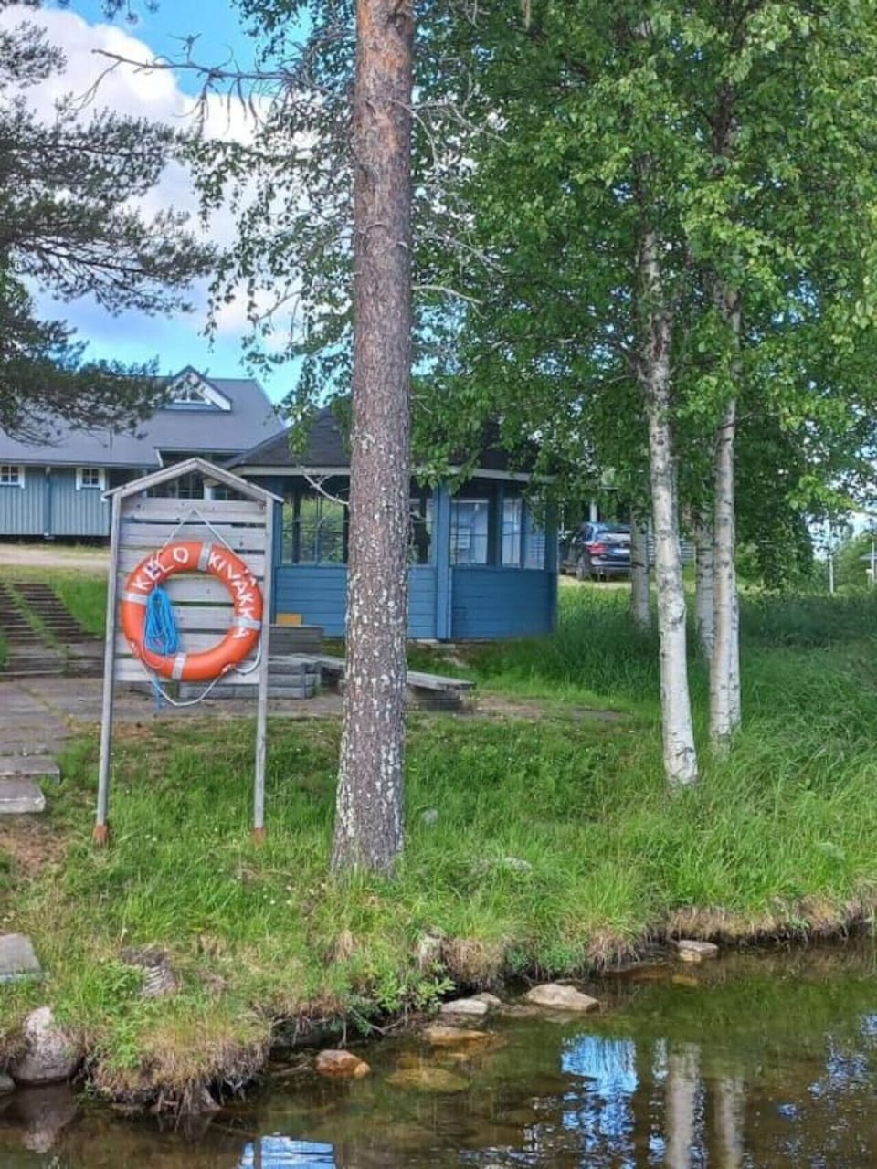 Exterior of the building in summer, with birch trees and a parking space beside it.