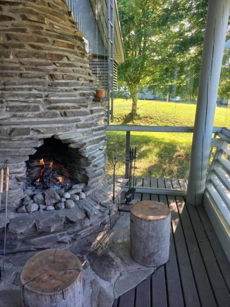 Stone fireplace lit on the enclosed terrace, with a view out to the lawn.