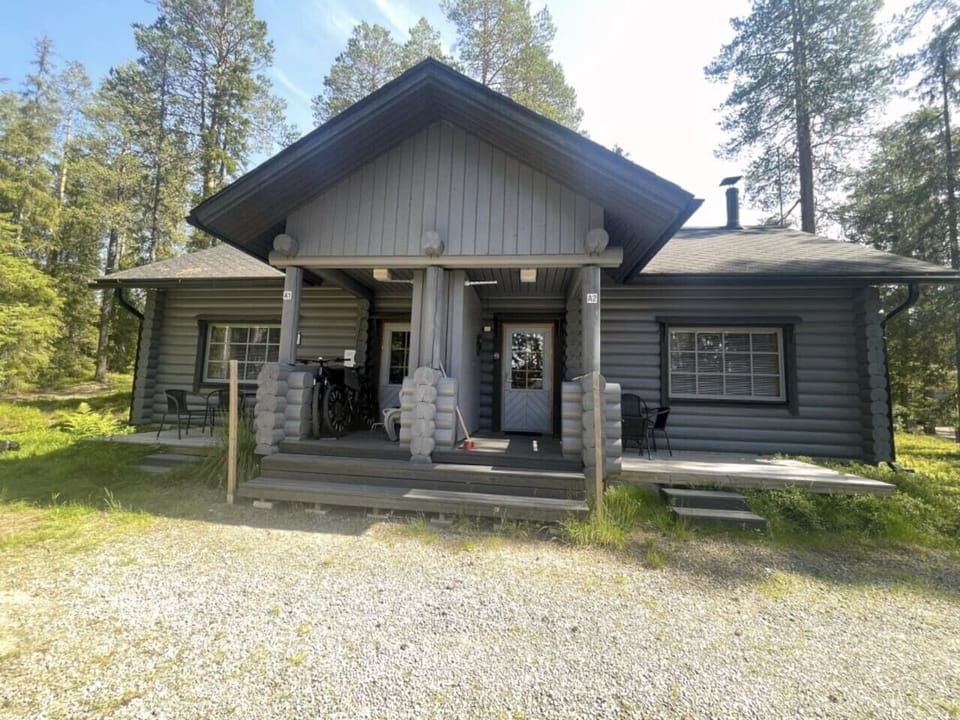 Traditional round-log cabin exterior with a covered porch and outdoor seating in a peaceful forest setting.