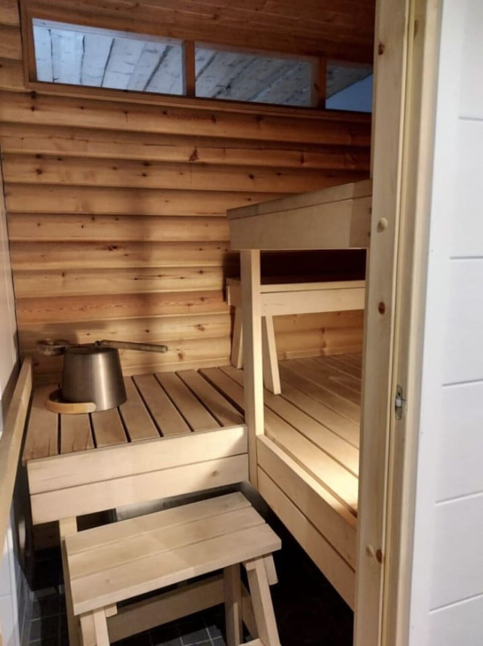 Electric sauna with wooden benches and a water bucket, ready for a relaxing steam.