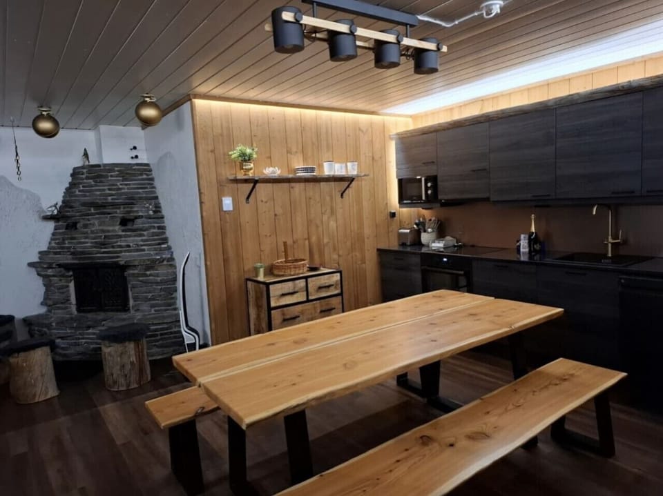 Long wooden dining table with bench seating next to the fireplace and kitchen.
