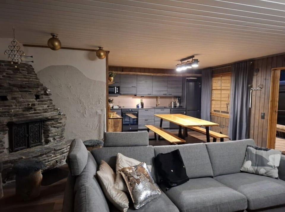 Open-plan living room and kitchen with a stone fireplace, comfortable sofa and a large dining table.