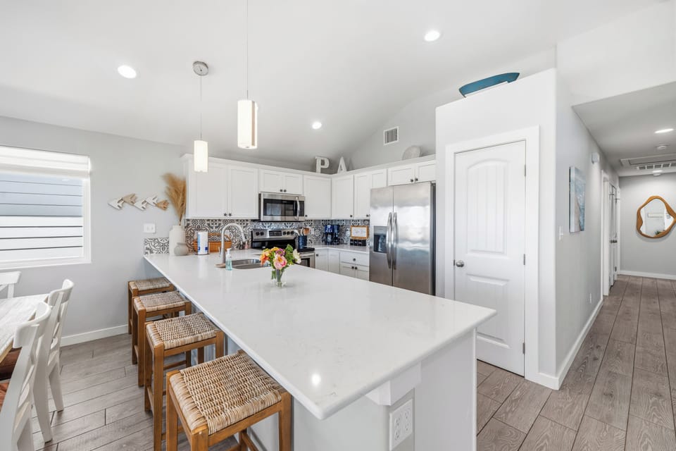 Step into your bright, modern kitchen with sleek white cabinetry, a spacious island for gathering, and stainless steel appliances—a welcoming space to cook, share meals, and create vacation memories.