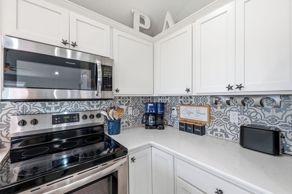Your bright, fully equipped kitchen features crisp white cabinetry, modern stainless appliances, and charming patterned tile backsplash. Everything you need for easy meal prep and your morning coffee awaits.