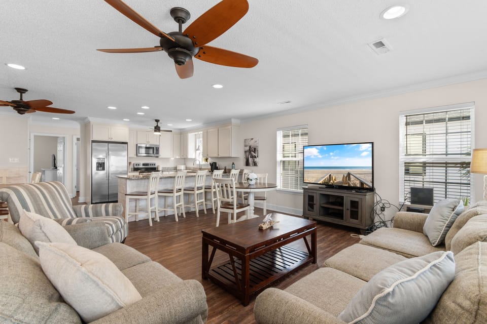 Relax in your spacious open-concept living area featuring comfortable seating, ceiling fans, and modern kitchen—perfect for family gatherings.