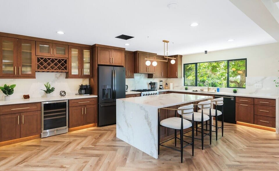 Modern, aesthetic kitchen is featured with cabinetry, marble-topped island with seating, and stainless steel appliances that offer both functionality and style for cooking. 