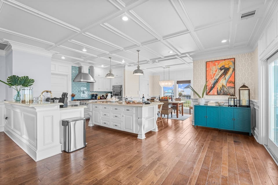 Beautiful coastal kitchen featuring a large center island, modern appliances, ample cabinetry, pendant lighting, and an open dining area.