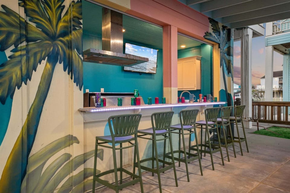 Beach house outdoor bar featuring counter seating, tropical wall art, and a convenient covered setting for drinks and casual gatherings.
