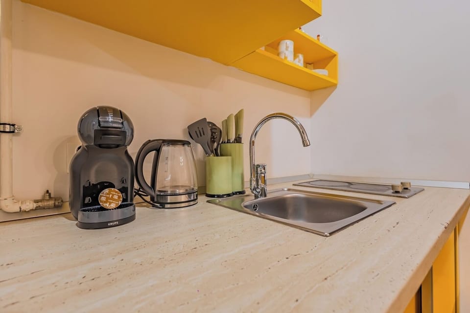 Kitchen worktop with Dolce Gusto coffee machine and capsules provided, electric kettle and stainless steel sink. Yellow open shelving with cups and kitchen essentials. Maia Studio in Old Town, Brasov.