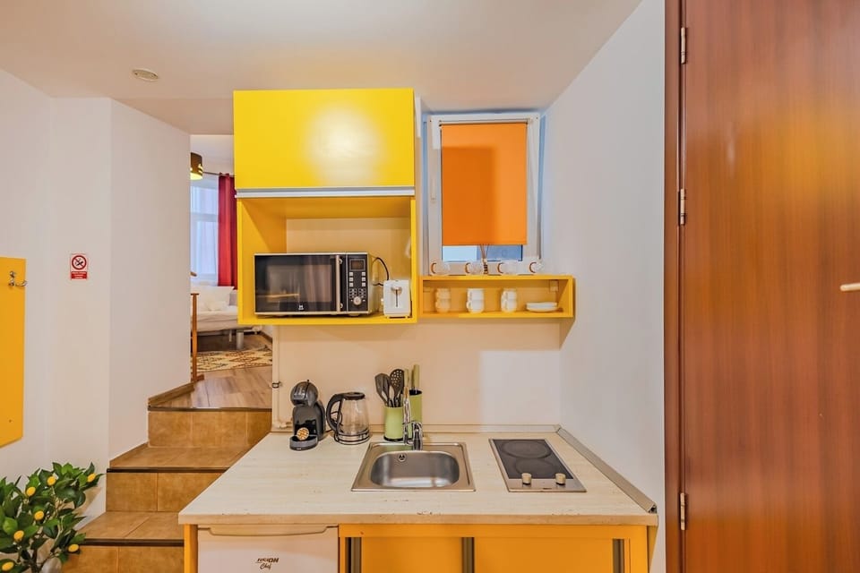 Bright kitchen with bold yellow cabinetry, 2-ring induction hob, microwave, coffee machine, electric kettle and toaster. Mini fridge below the worktop. Maia Studio in Old Town, Brasov, sleeps 3.