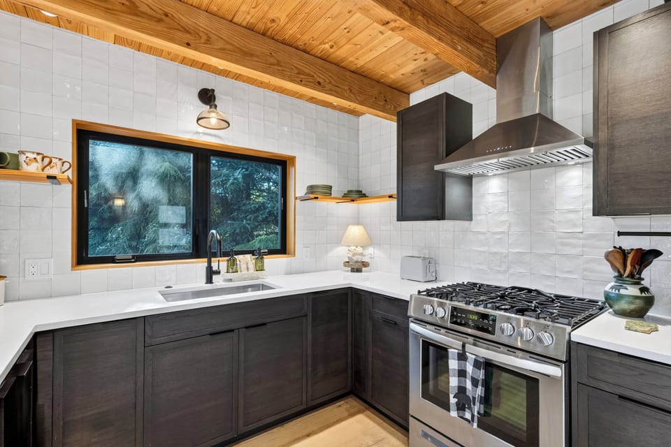 Well-appointed kitchen with a gas range, dark cabinetry, and a forest-facing window above the sink.