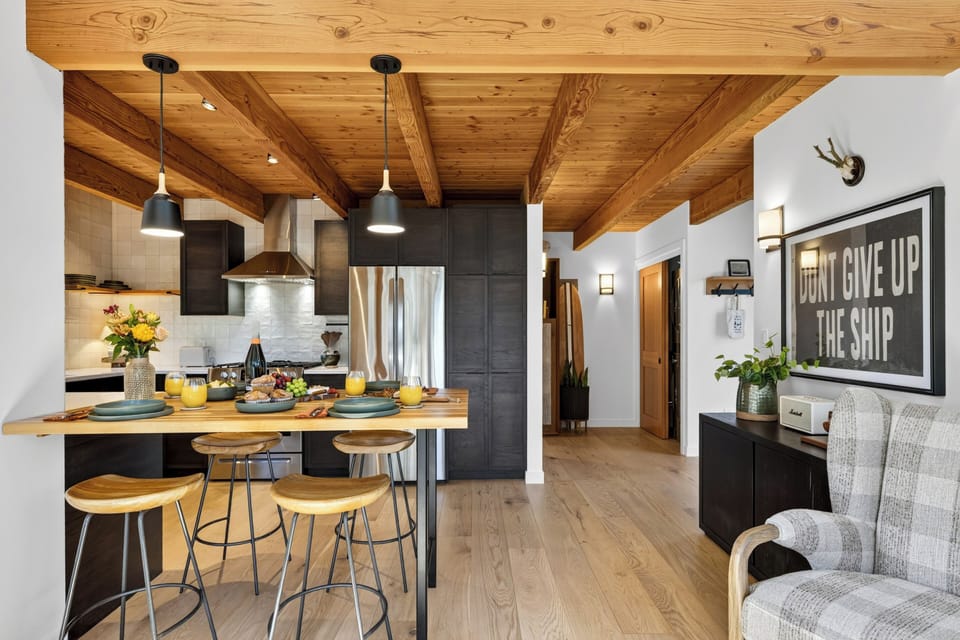 Warm kitchen entry with breakfast bar seating, wood-beamed ceilings, and cozy coastal cabin character.
