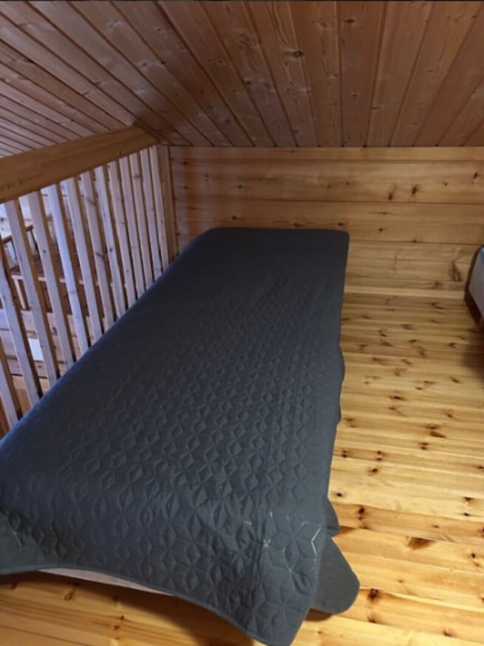 Single bed in the loft beside the wooden railing.