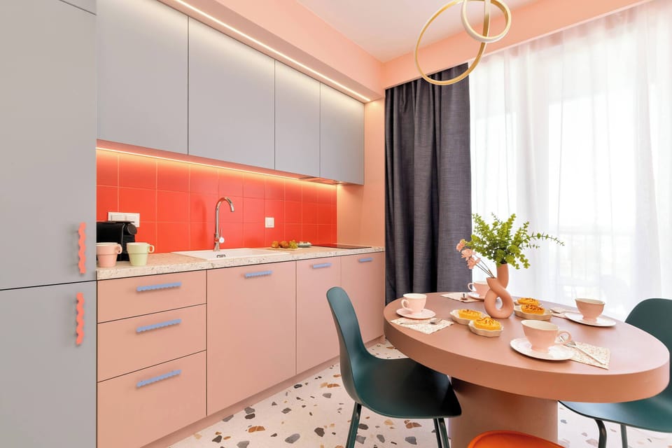A modern kitchenette with pink cabinets, orange backsplash, and a small dining area.