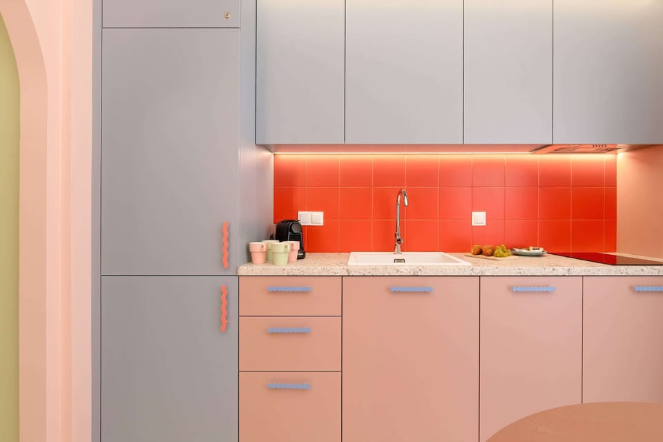 A bright kitchen with pink cabinets, orange backsplash, and built-in appliances.
