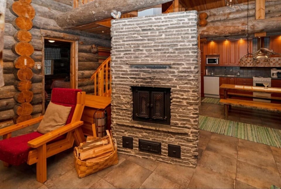 Living area with a large fireplace and a wooden armchair, with the kitchen just behind.