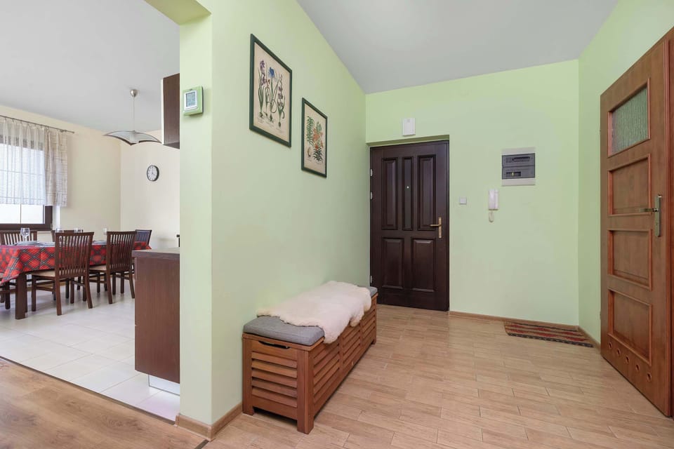An inviting entrance hallway features soft green walls, framed wall art, and warm wooden flooring. A compact entryway bench provides a practical spot for putting on shoes.