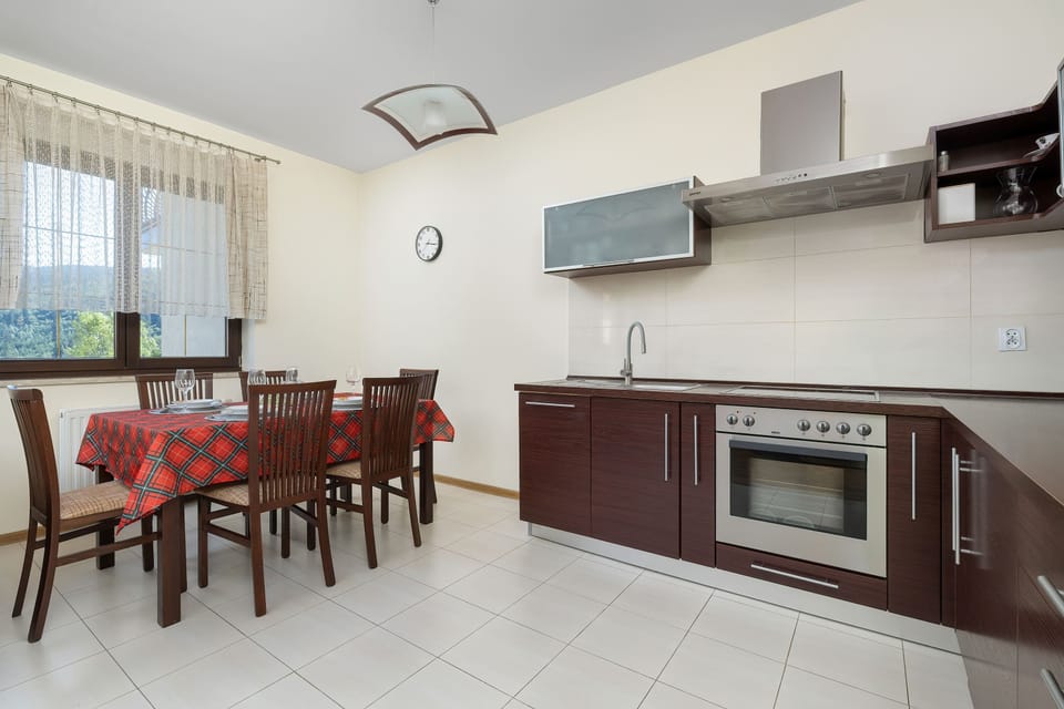 A spacious dining space contains a large dark wooden dining table surrounded by matching chairs. In the background, dark wooden kitchen cabinetry extends along the tiled walls.