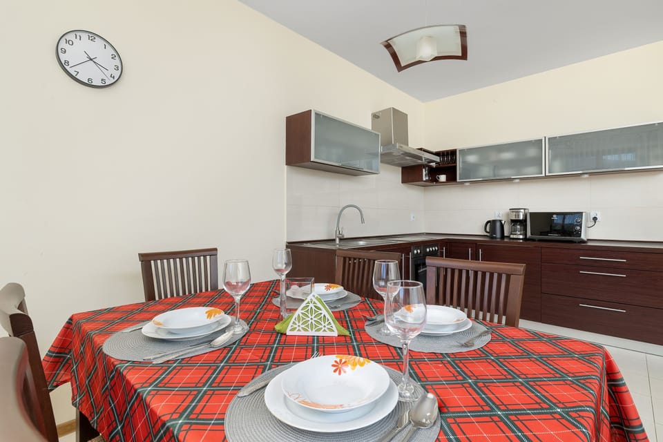 A dining table is set with plates, glassware, and an orange patterned tablecloth under ambient ceiling lighting. The open kitchenette area in the background provides easy access for serving meals.