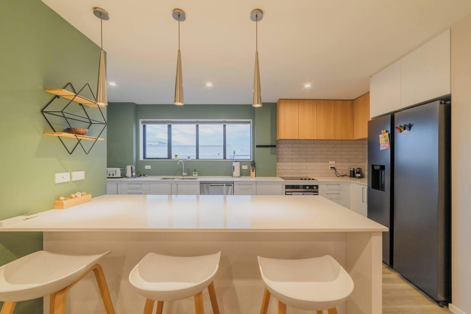Contemporary kitchen featuring a spacious breakfast island, three visible stools, ample storage and a large side-by-side fridge-freezer.