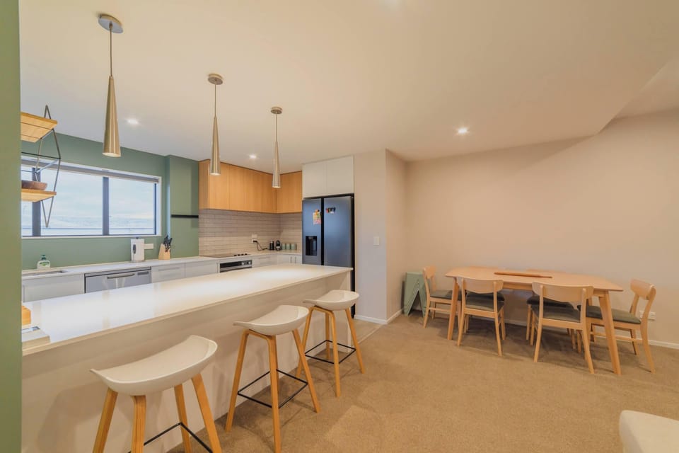 Open-plan kitchen and dining area with four breakfast stools, pendant lighting and a six-seat dining table in Christchurch Central City.