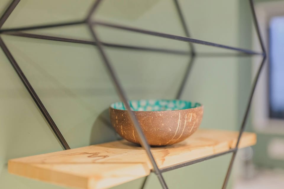 Modern geometric wall shelf with timber ledges and a decorative bowl adds character to the green kitchen feature wall.