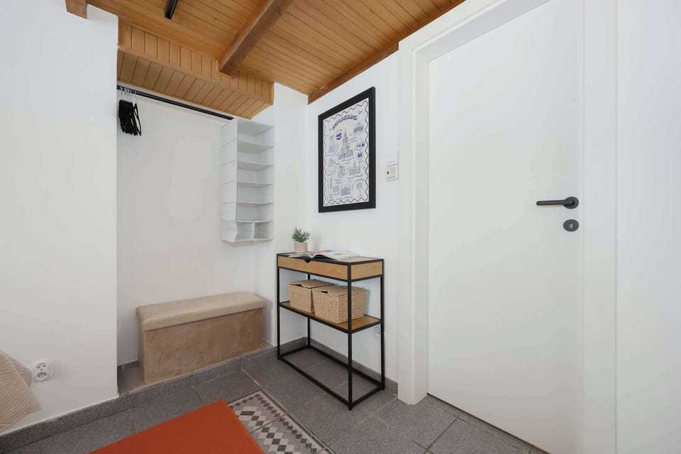 The bright apartment entryway features a console table, bench, and white door set beneath a wood-paneled ceiling.