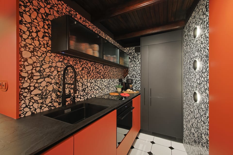A kitchen corner combines vibrant terracotta-colored cabinets with a black countertop and a bold patterned backsplash. Modern black fixtures add contrast.