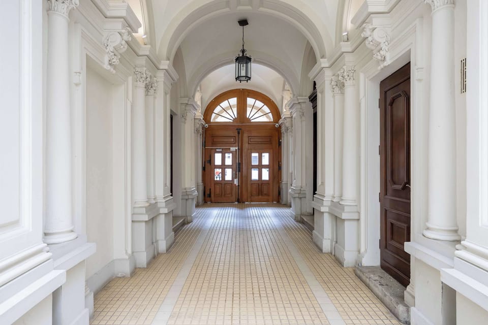 An elegant vaulted entrance hallway in a historic building displays classical white arches, decorative pillars, and tiled floors.