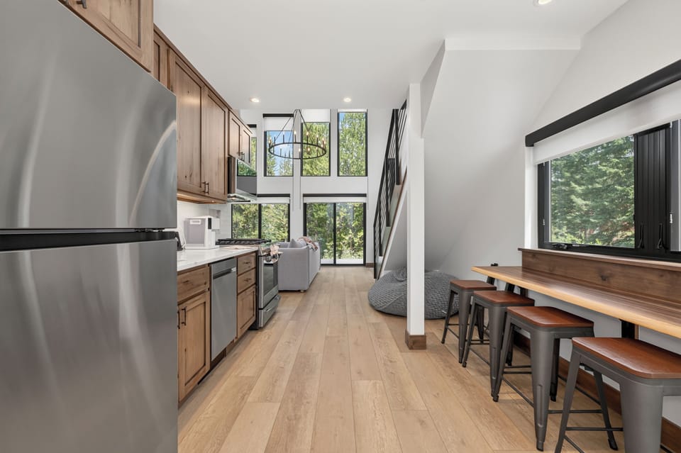 Step into a bright, modern retreat where soaring ceilings and floor-to-ceiling windows frame lush forest views. Your fully equipped kitchen opens to a welcoming living area, perfect for cooking, gathering, and unwinding in natural light.