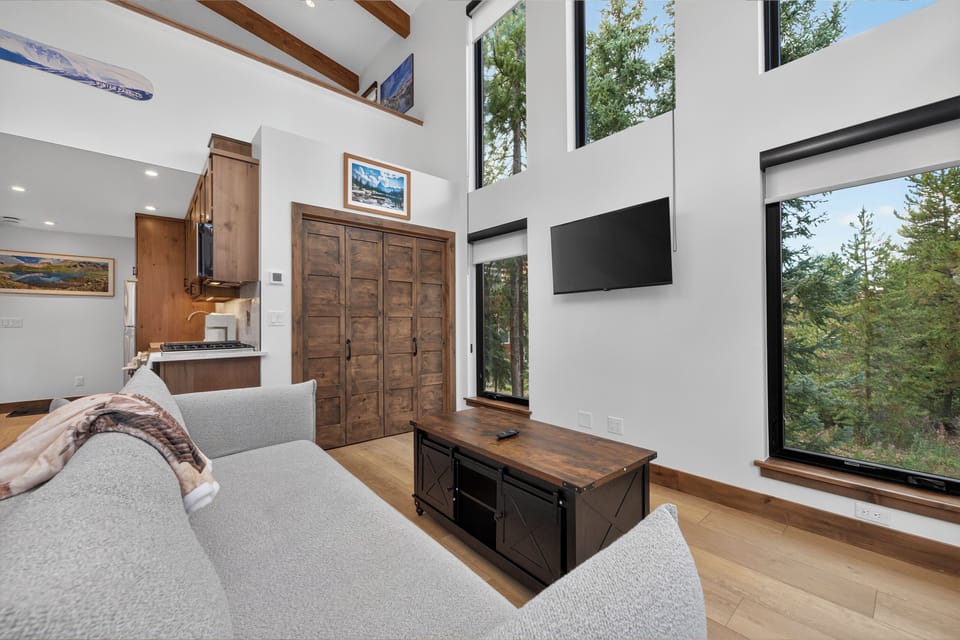 Relax in your light-filled living space, where soaring ceilings and floor-to-ceiling windows frame peaceful forest views. The cozy sectional invites you to unwind after a day exploring the mountains.