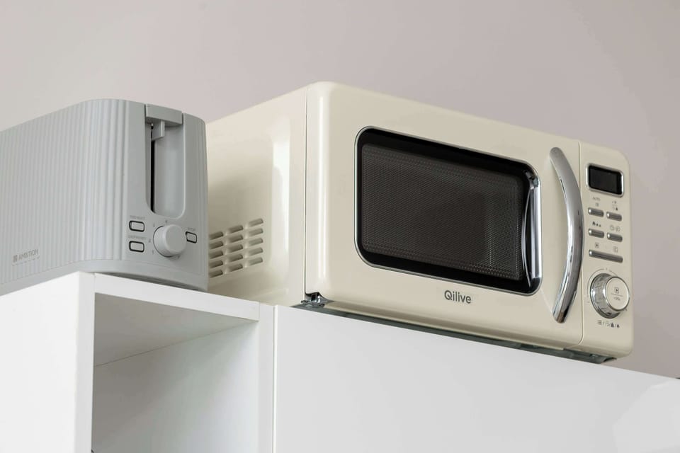 A close-up shot focuses on a retro-style cream microwave and a matching toaster sitting on top of white kitchen cabinetry.