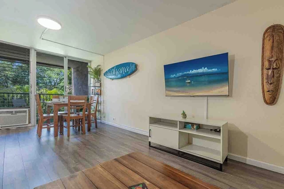 Light-filled living and dining area with tropical décor. Sliding doors open to a private lanai overlooking lush greenery.