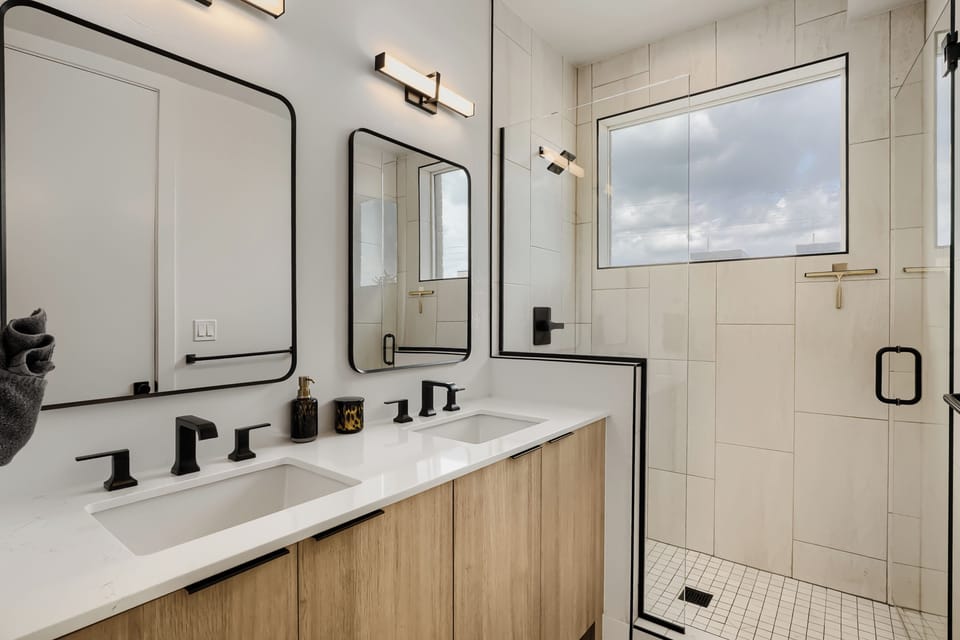 Refresh in your bright modern bathroom with dual vanities and a spacious walk-in shower featuring sleek black fixtures and natural light streaming in.